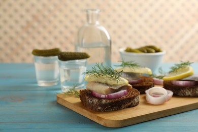 Delicious sandwiches with salted herring, lemon, onion rings and dill on light blue wooden table. Space for text