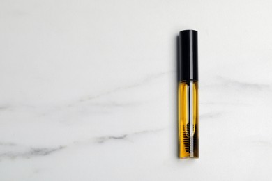Photo of Tube of eyelash oil on white marble table, top view. Space for text