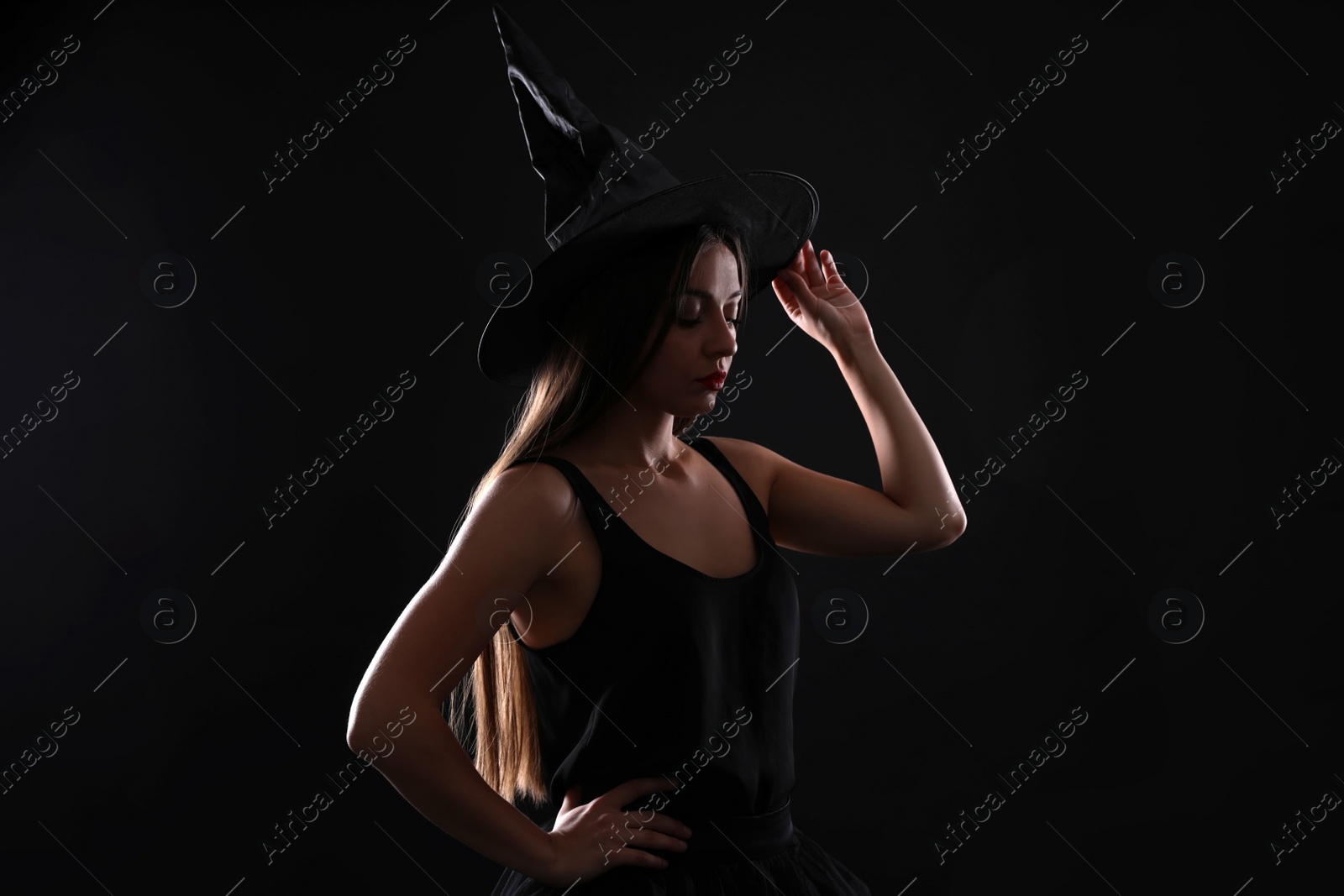 Photo of Young woman wearing witch costume on black background, space for text. Halloween party