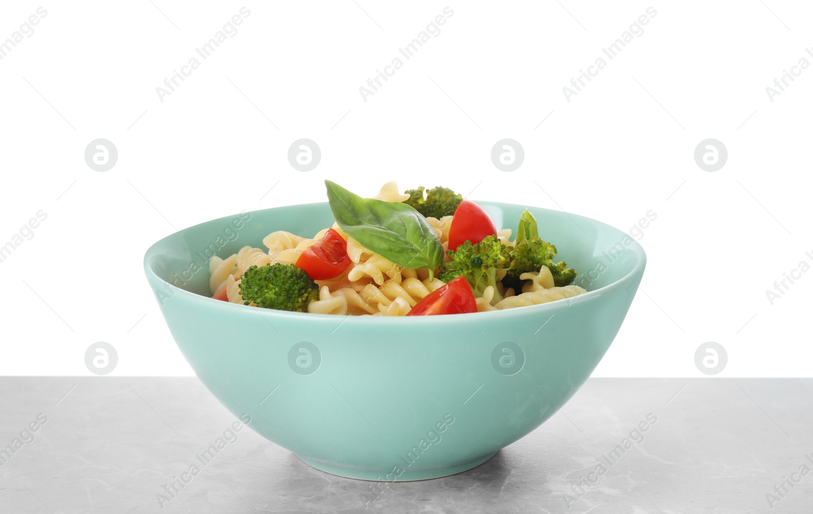 Photo of Tasty pasta with broccoli, cherry tomatoes and basil on light grey marble table against white background