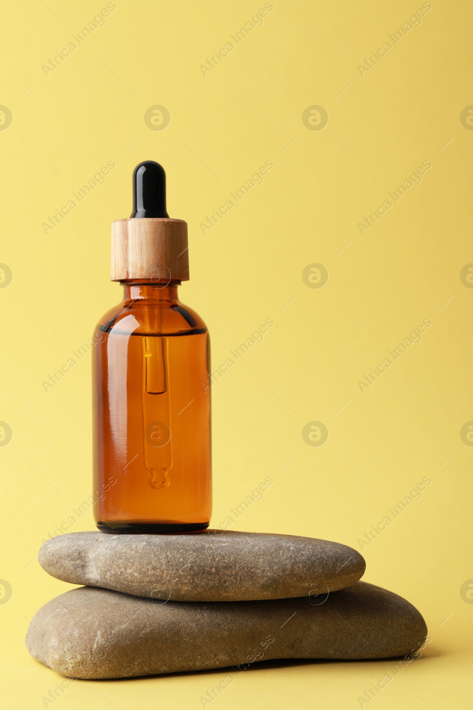 Photo of Bottle of face serum and spa stones on yellow background