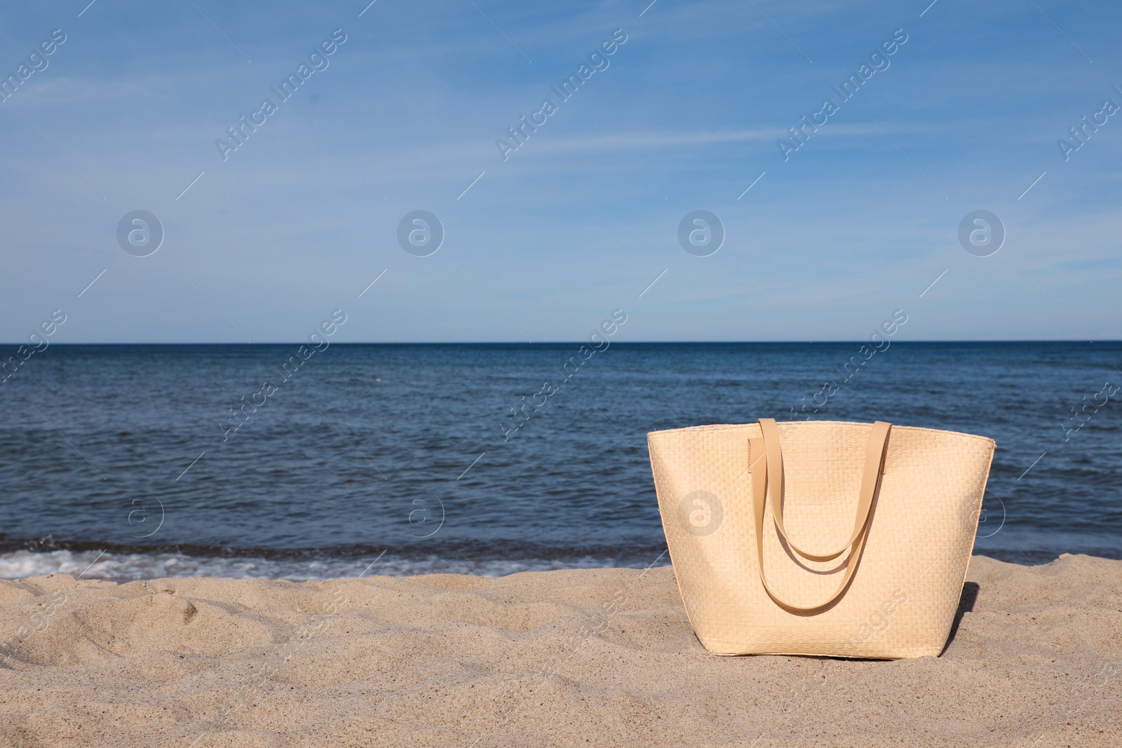 Photo of Stylish summer bag on sand near sea, space for text. Beach accessory