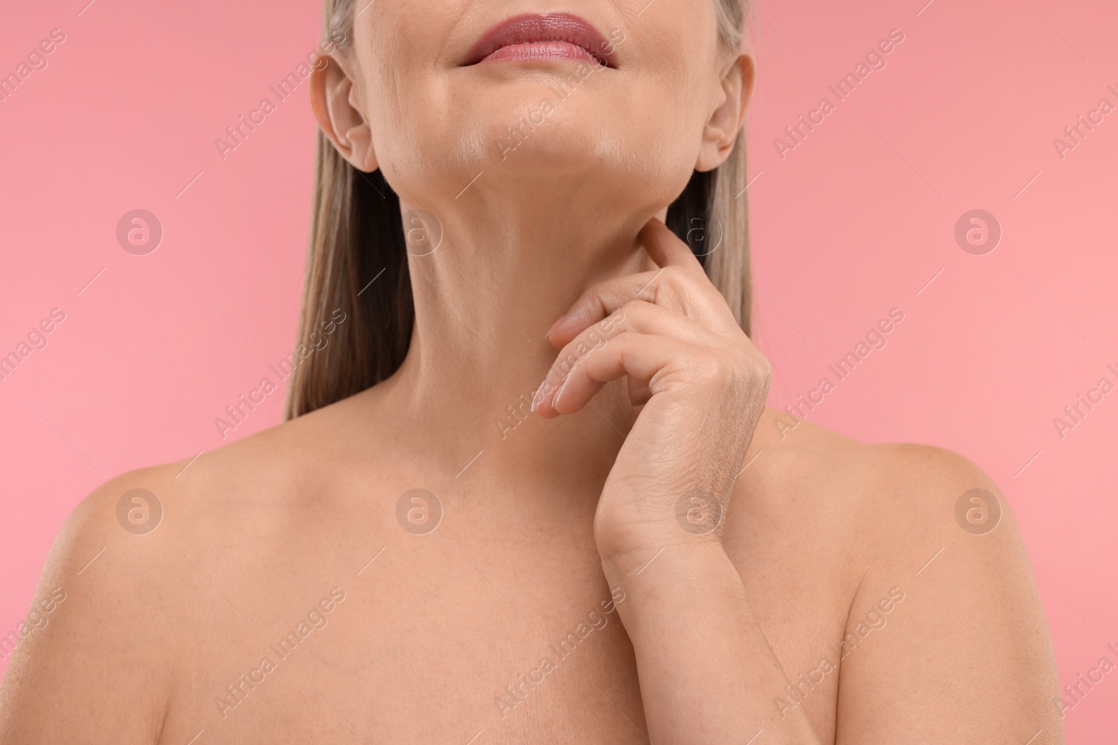 Photo of Mature woman touching her neck on pink background, closeup