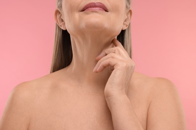 Mature woman touching her neck on pink background, closeup