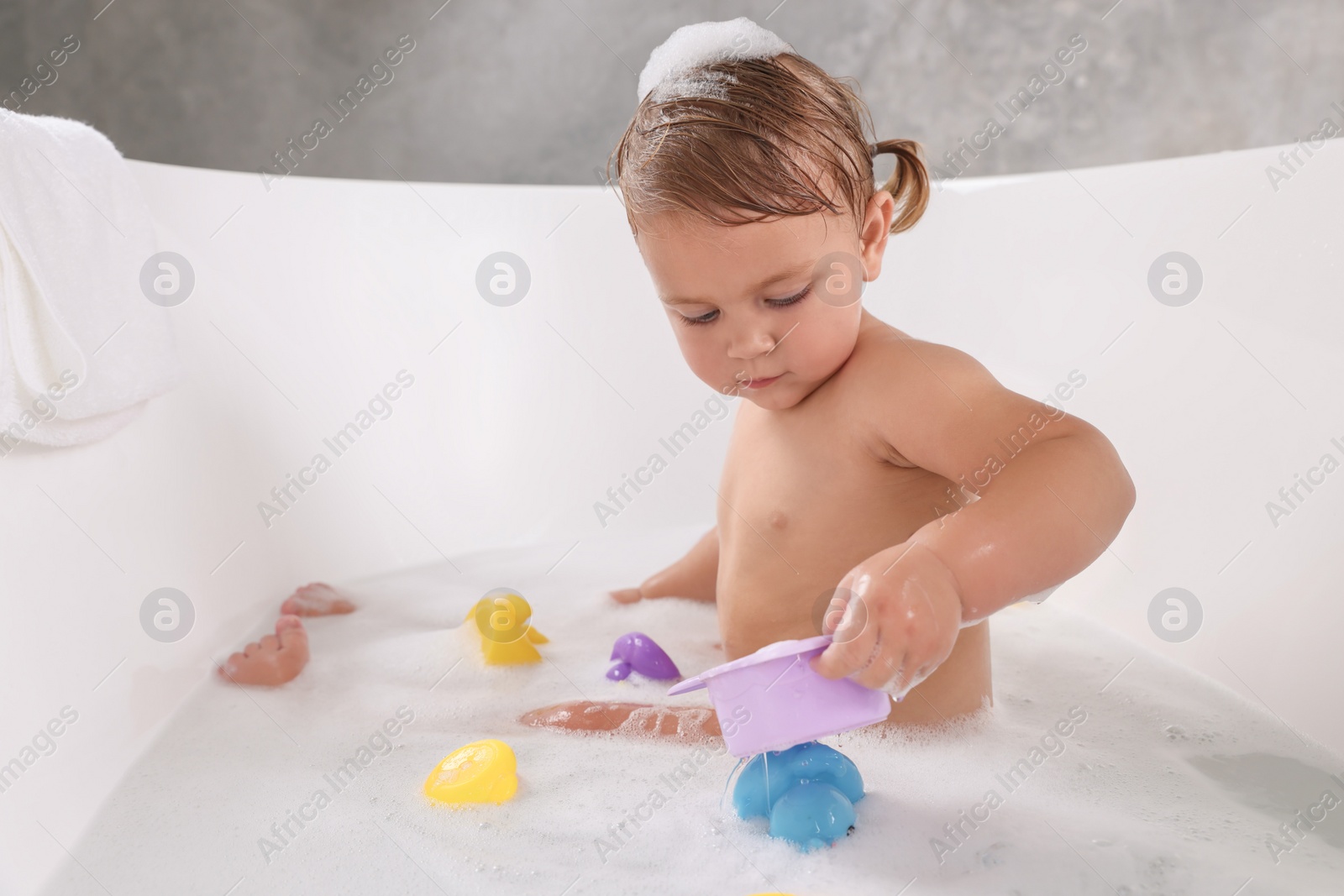 Photo of Cute little girl taking bubble bath with toys indoors