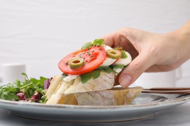 Photo of Woman taking tasty bruschetta with tomatoes, mozzarella and olives from plate, closeup