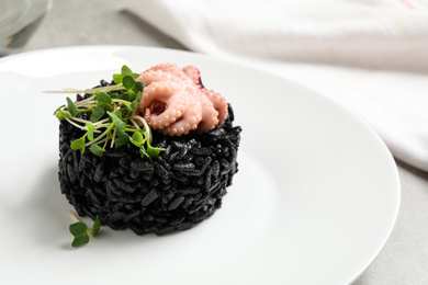 Photo of Delicious black risotto with baby octopus in plate, closeup