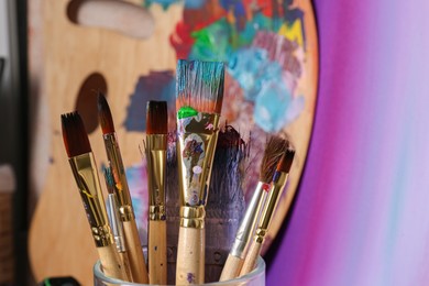 Brushes with colorful paints and wooden artist's palette, closeup. Space for text