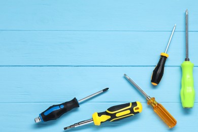 Group of different screwdrivers on light blue wooden table, top view