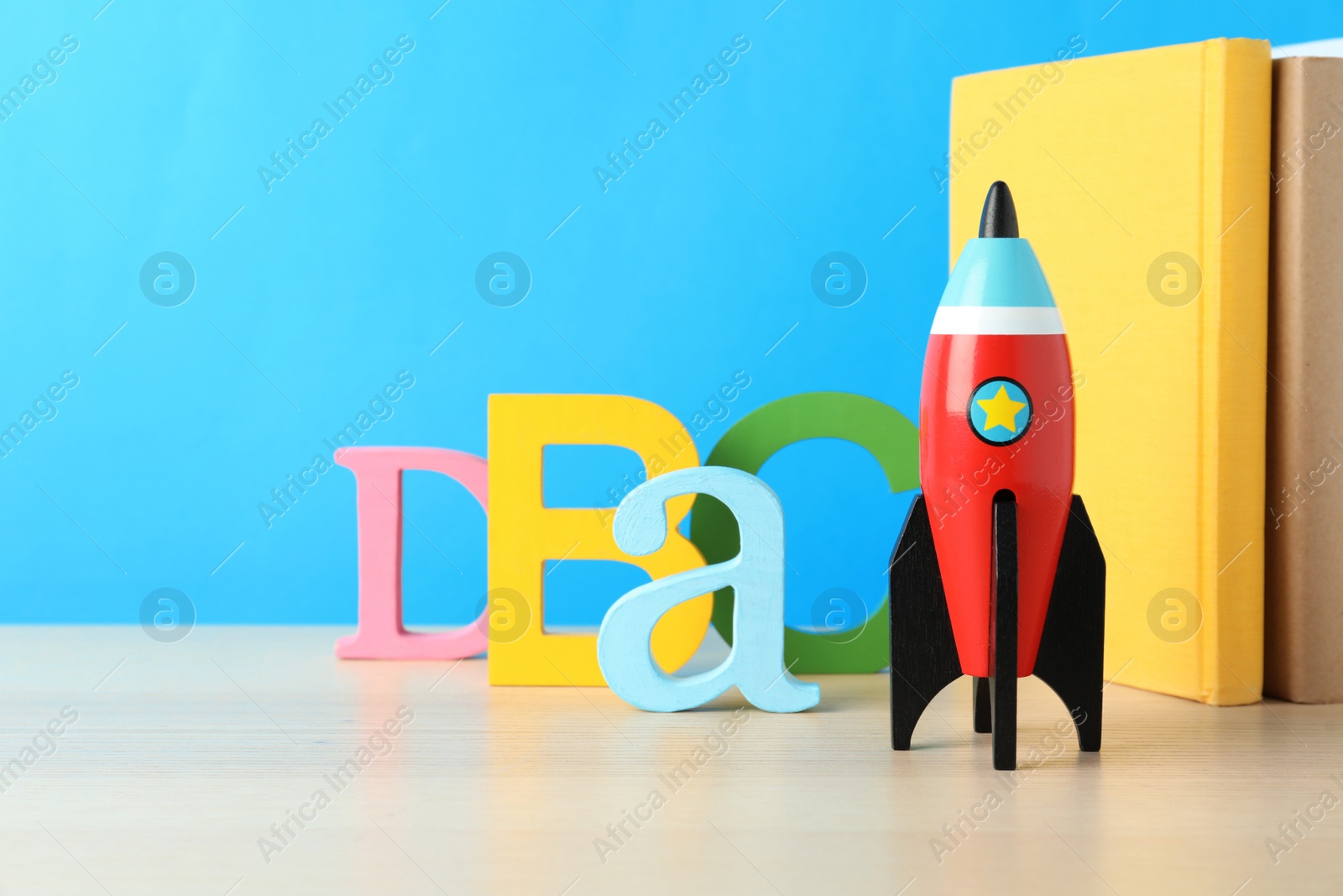 Photo of School books and rocket on wooden table against light blue background