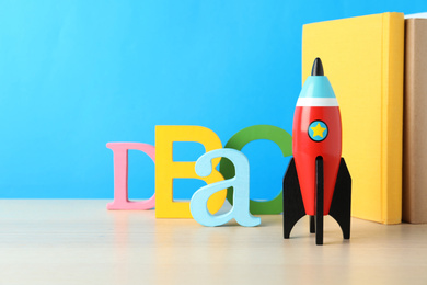 School books and rocket on wooden table against light blue background