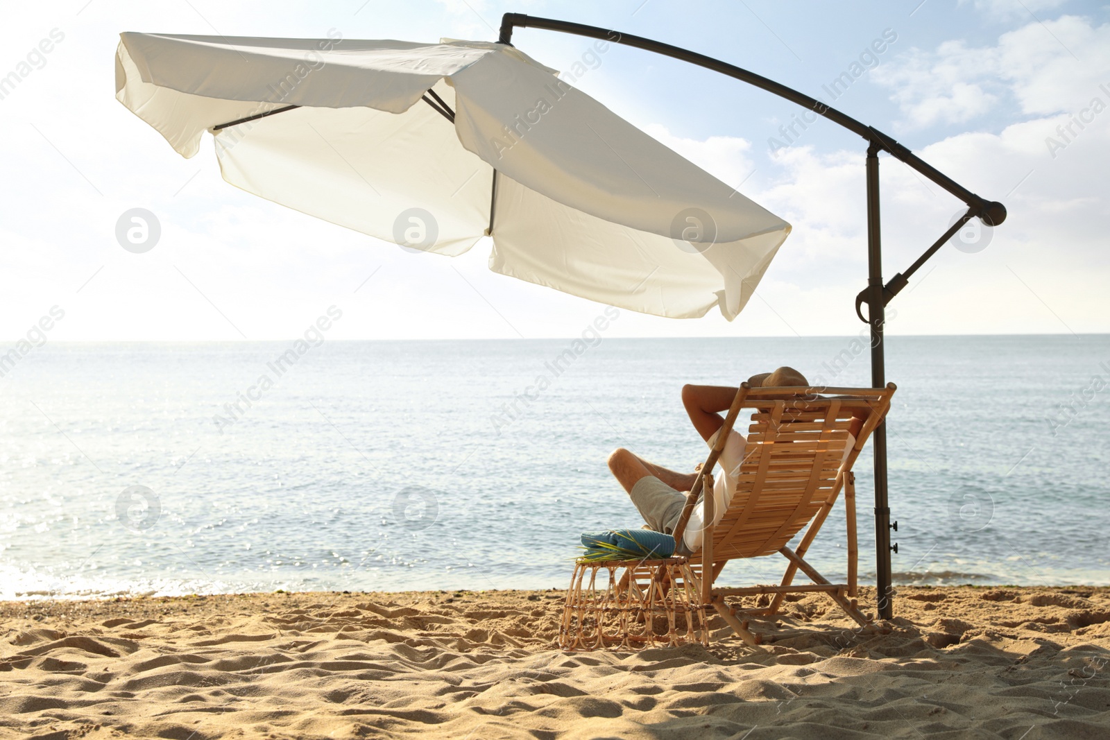 Photo of Man relaxing on deck chair at sandy beach. Summer vacation