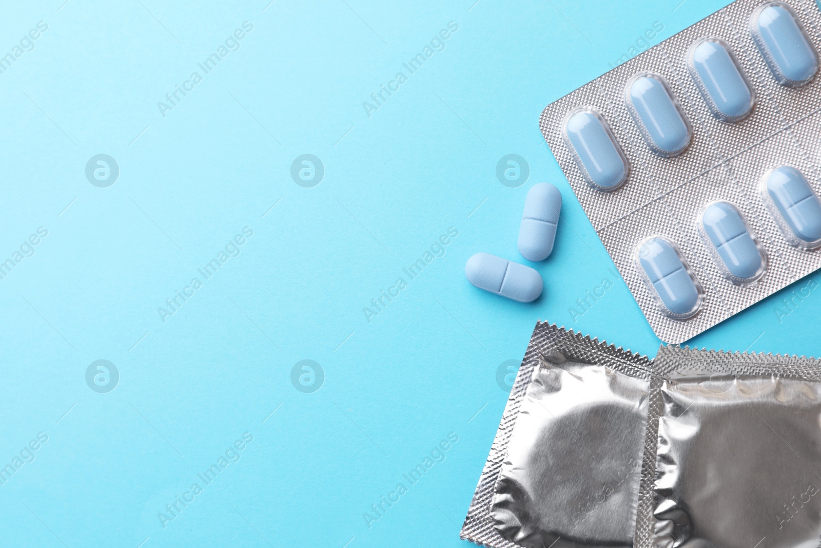 Photo of Pills and condoms on light blue background, flat lay with space for text. Potency problem