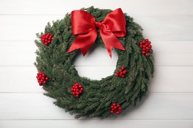 Beautiful Christmas wreath with red berries and bow on white wooden background