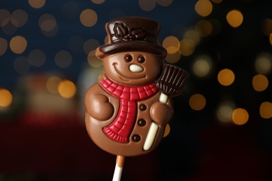 Funny chocolate snowman candy against blurred festive lights, closeup