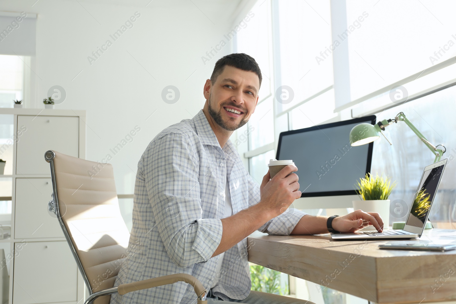 Photo of Freelancer with cup of coffee working on laptop at table indoors