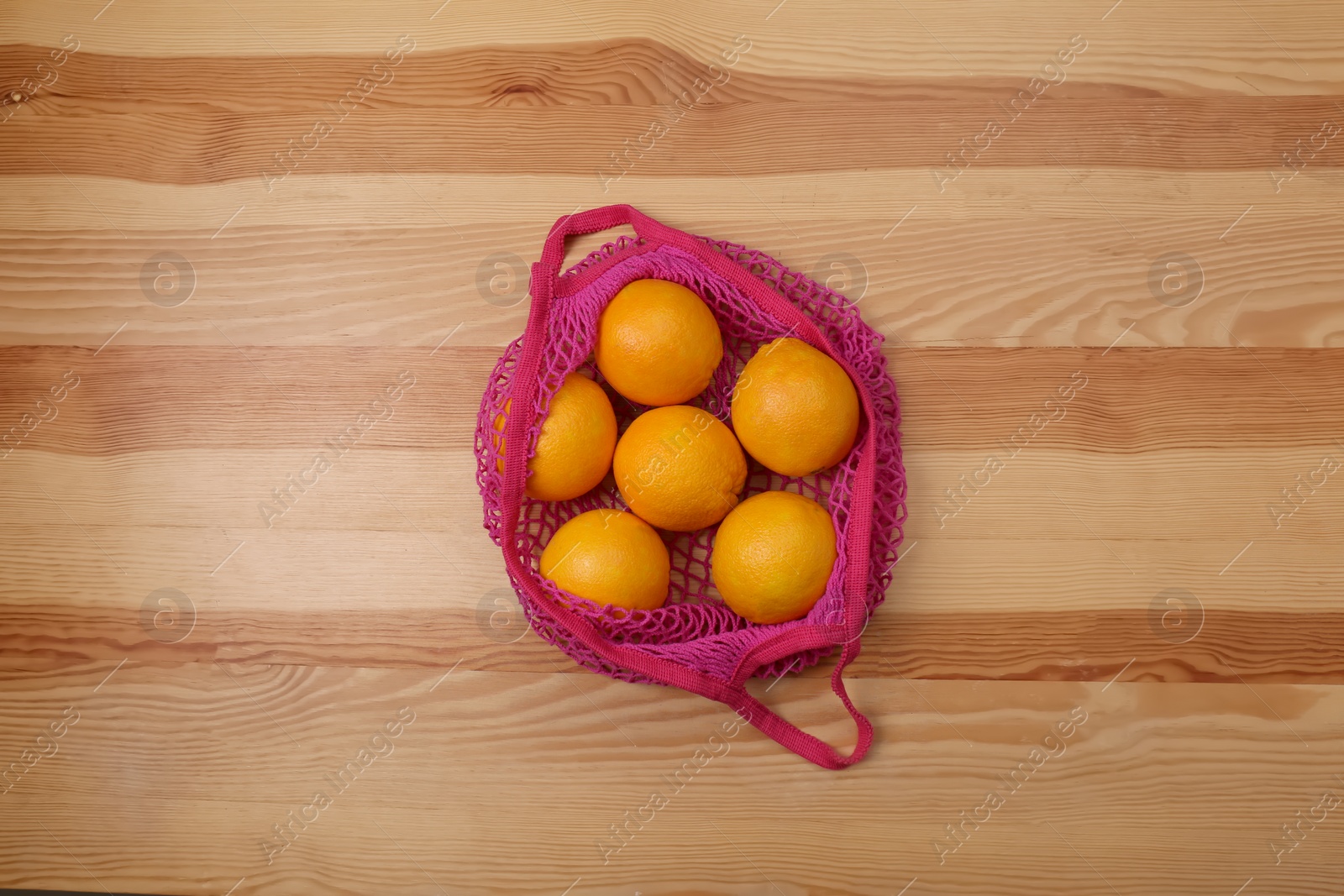 Photo of Pink net bag with oranges on wooden background, top view