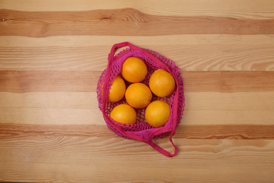Photo of Pink net bag with oranges on wooden background, top view