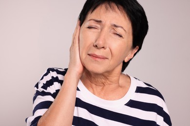 Senior woman suffering from ear pain on light grey background