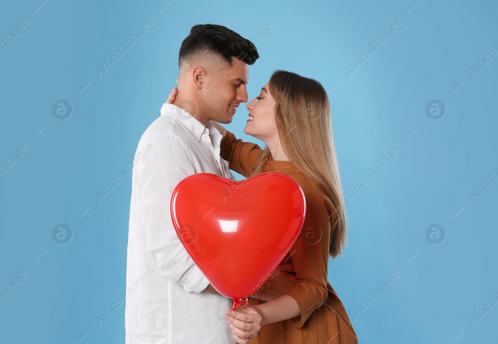 Photo of Lovely couple with heart shaped balloon on light blue background. Valentine's day celebration