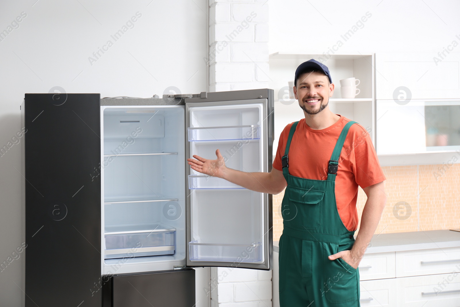 Photo of Male technician in uniform near refrigerator indoors