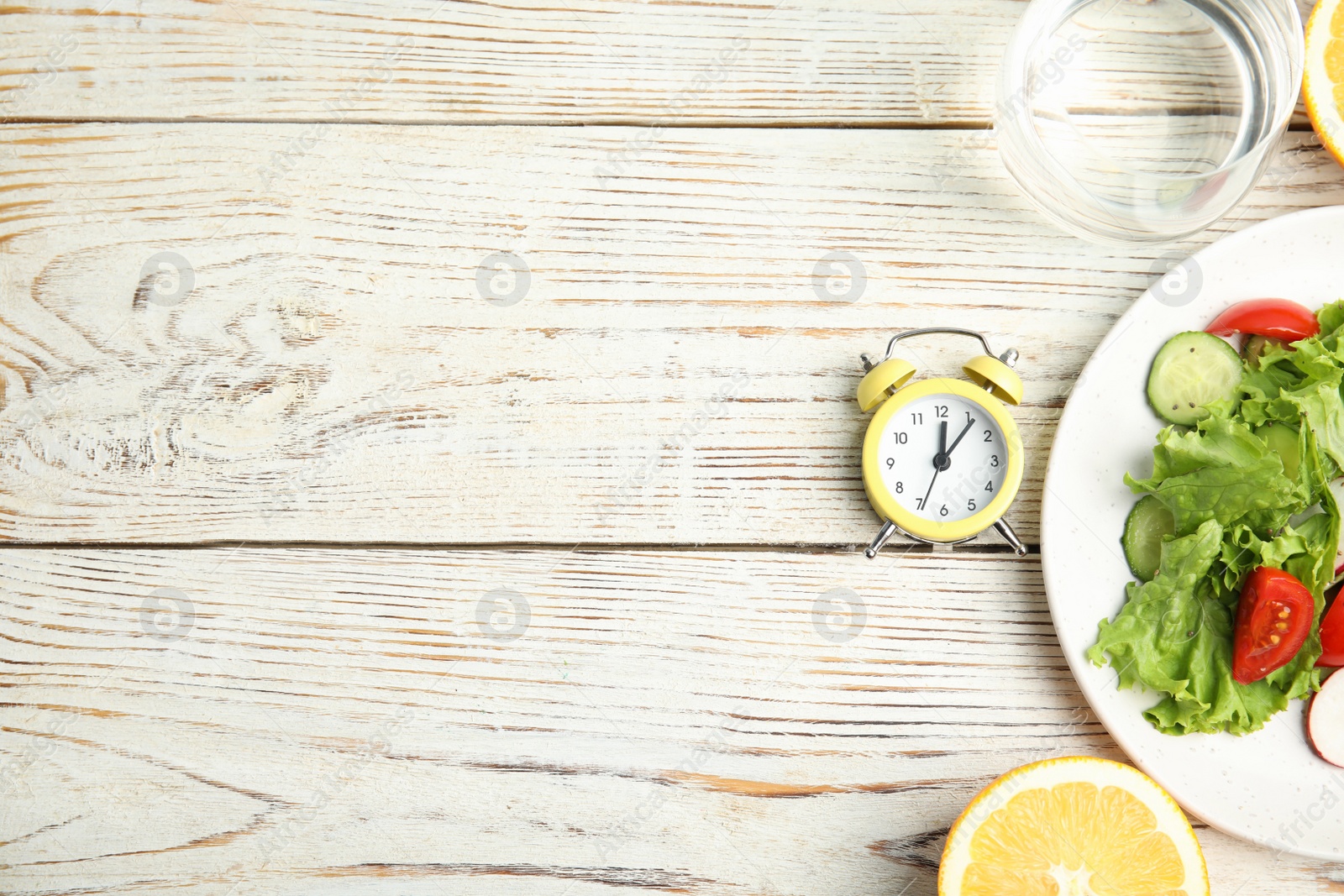 Photo of Alarm clock and healthy food on white wooden table, flat lay with space for text. Meal timing concept