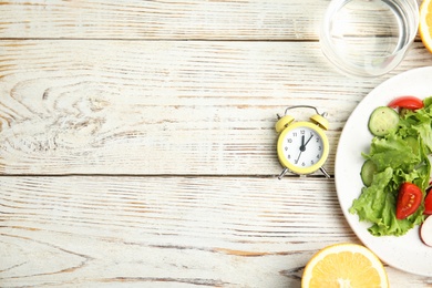 Photo of Alarm clock and healthy food on white wooden table, flat lay with space for text. Meal timing concept