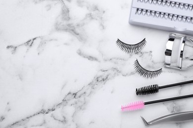 Photo of Flat lay composition with false eyelashes and tools on white marble table. Space for text