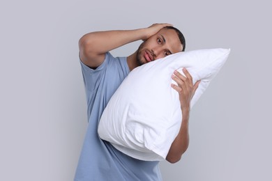 Photo of Sleepy man with pillow on light grey background. Insomnia problem
