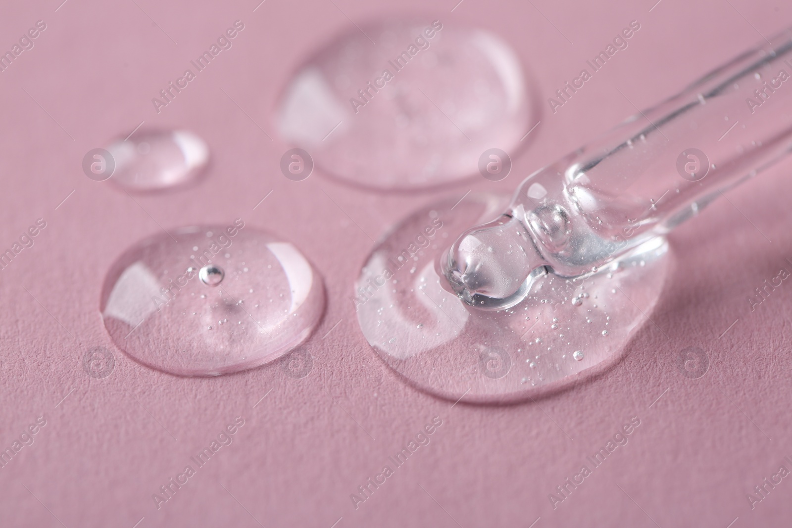 Photo of Dripping cosmetic serum from pipette onto pink background, macro view