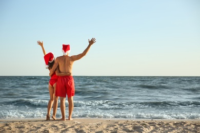 Photo of Lovely couple with Santa hats together on beach, back view. Christmas vacation