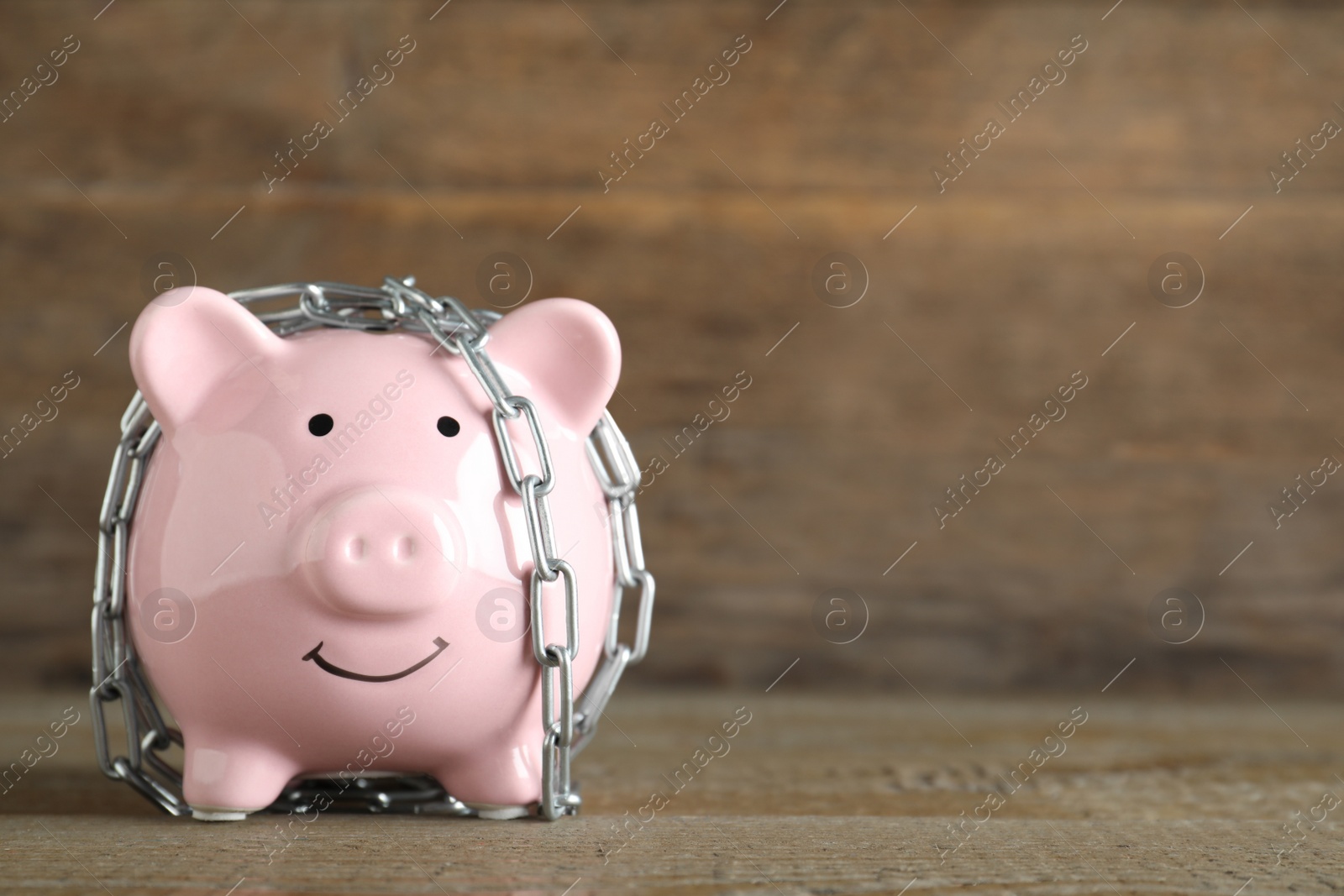 Photo of Piggy bank with steel chain on wooden table, space for text. Money safety concept