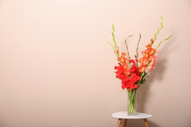 Photo of Vase with beautiful gladiolus flowers on wooden table against beige background. Space for text