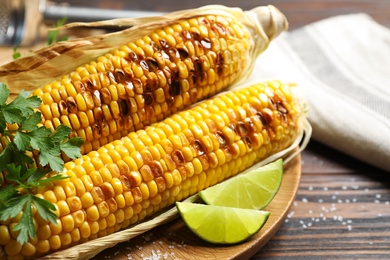 Photo of Delicious grilled corn cobs on wooden table, closeup