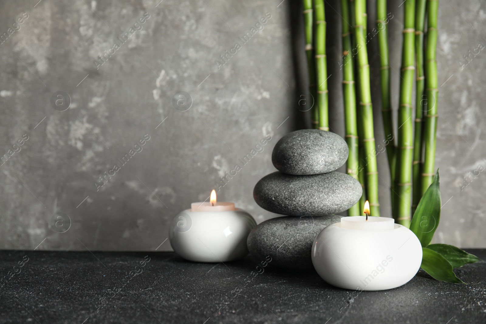 Photo of Spa stones with candles and bamboo on table, space for text