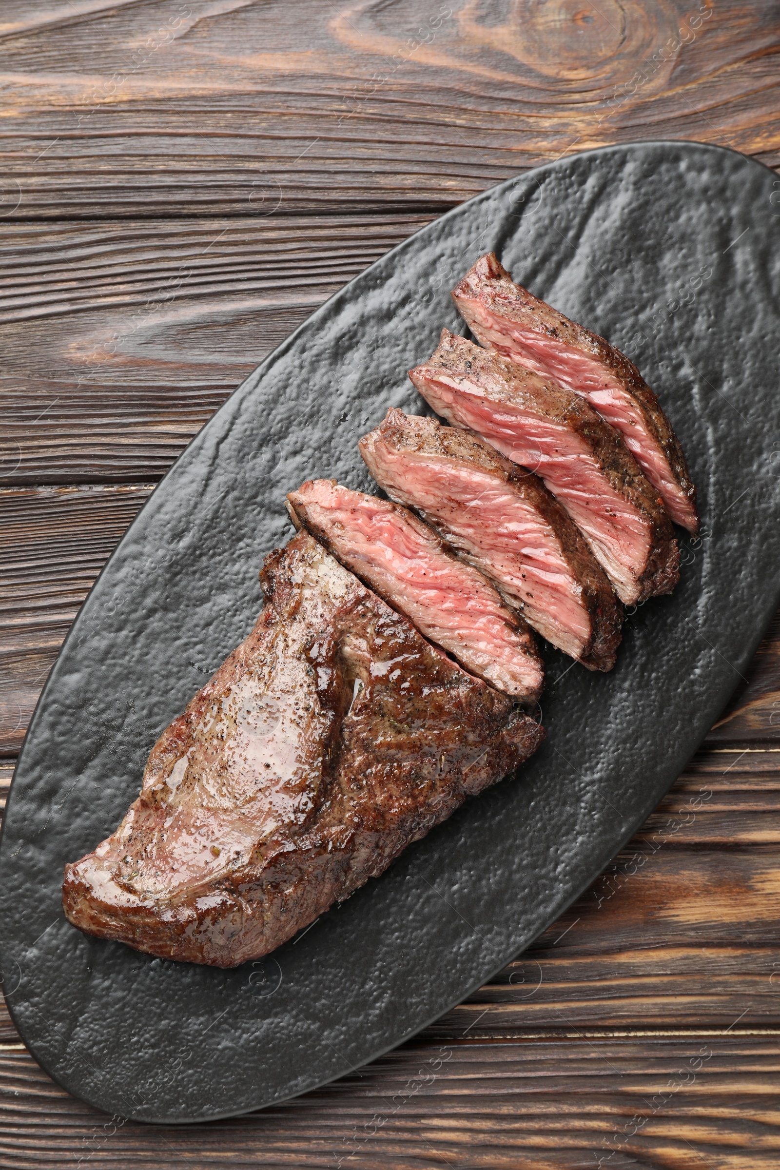 Photo of Pieces of delicious grilled beef meat on wooden table, top view