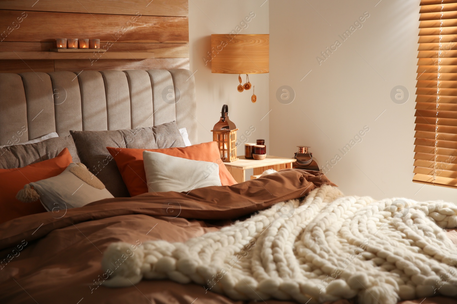 Photo of Cozy bedroom interior with knitted blanket and cushions