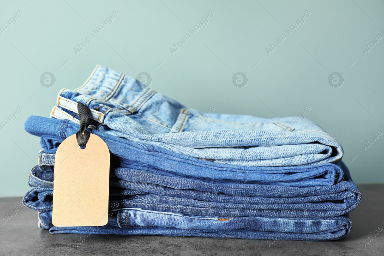 Photo of Stack of jeans on table against color background