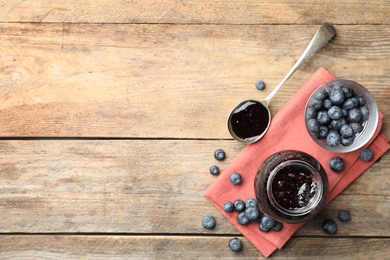 Jar of blueberry jam and fresh berries on wooden table, flat lay. Space for text
