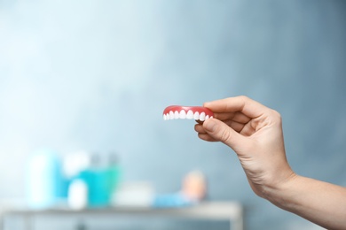 Woman holding teeth cover on blurred background. Space for text