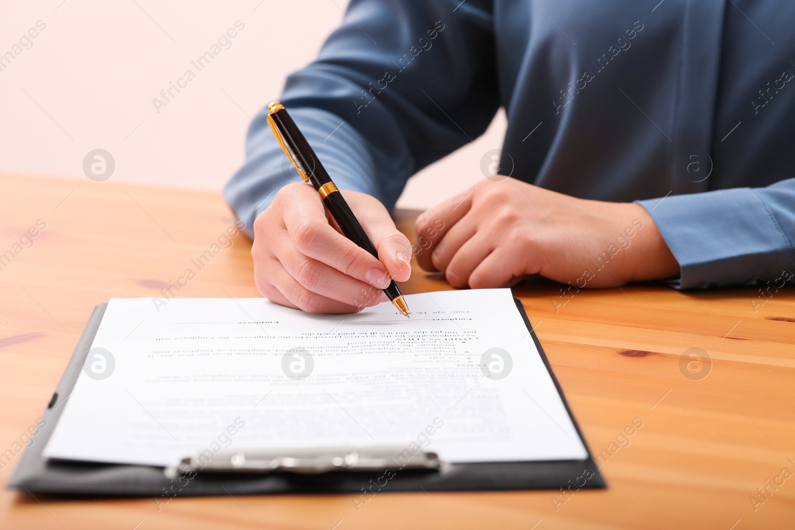 Photo of Businesswoman signing contract at wooden table, closeup of hands