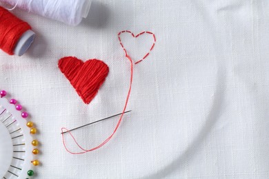 Photo of Embroidered red hearts and needle on white cloth, top view. Space for text