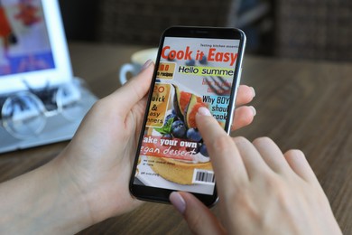 Photo of Woman reading online magazine on mobile phone at wooden table, closeup