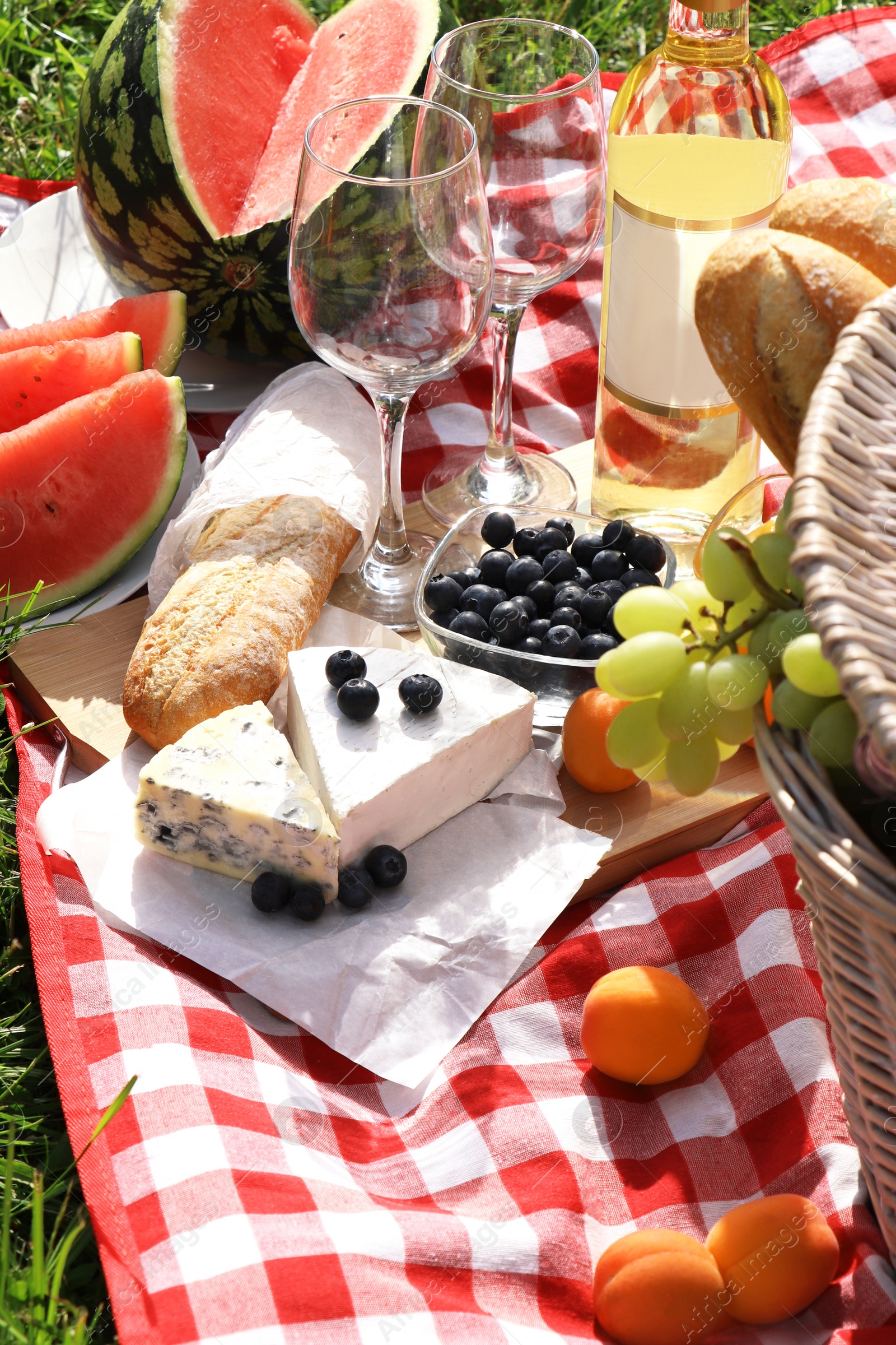 Photo of Picnic blanket with delicious food and wine outdoors on summer day