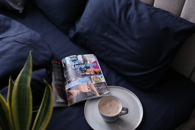 Open magazine and cup of coffee on bed with stylish silky linens, above view