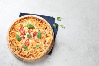 Tasty quiche with cheese, tomatoes and basil leaves on light grey table, top view. Space for text