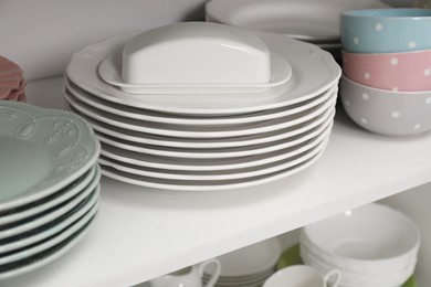 Photo of Clean plates, butter dish and bowls on shelf in cabinet indoors