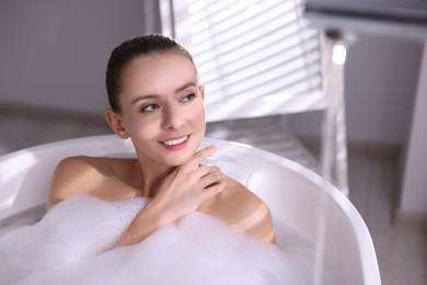 Photo of Beautiful woman taking bath in tub with foam indoors. Space for text
