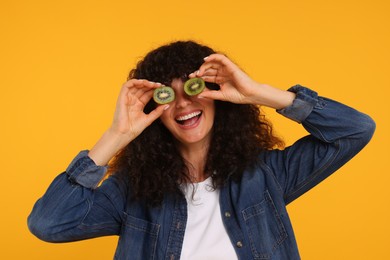 Photo of Woman covering eyes with halves of kiwi on yellow background