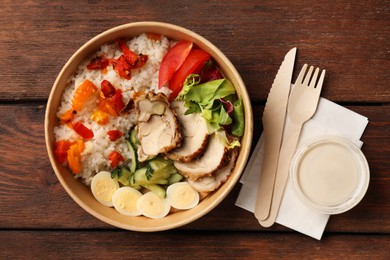 Photo of Tasty food in container with knife and fork on wooden table, flat lay